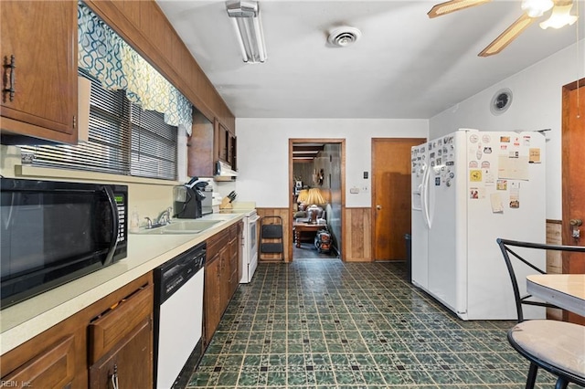 kitchen featuring ceiling fan, sink, wooden walls, and white appliances