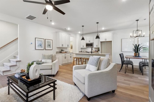 living room with ceiling fan with notable chandelier and light wood-type flooring