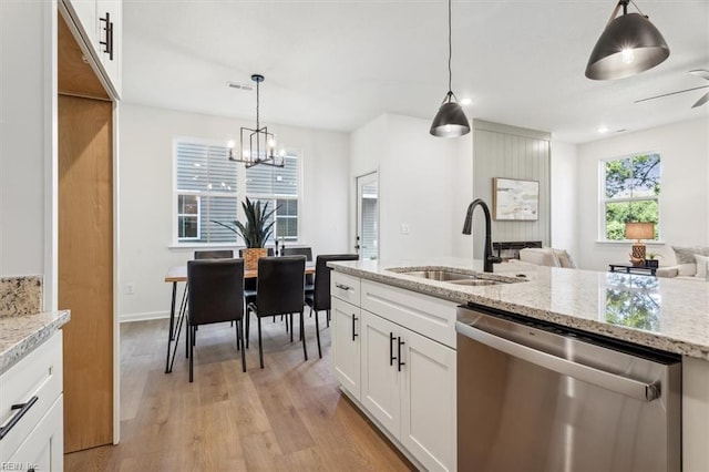 kitchen featuring pendant lighting, stainless steel dishwasher, sink, white cabinets, and light stone counters