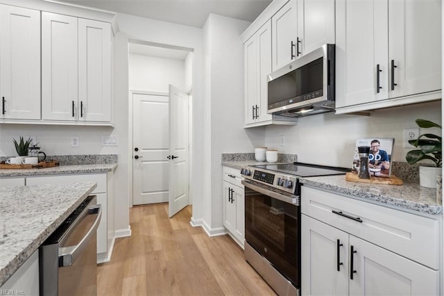 kitchen featuring light wood-type flooring, appliances with stainless steel finishes, light stone counters, and white cabinetry