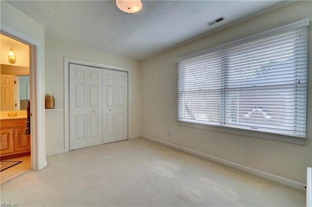 unfurnished bedroom featuring ensuite bath, light colored carpet, and a closet