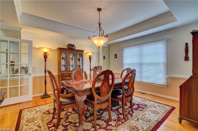 dining room featuring ornamental molding, light hardwood / wood-style flooring, and a tray ceiling