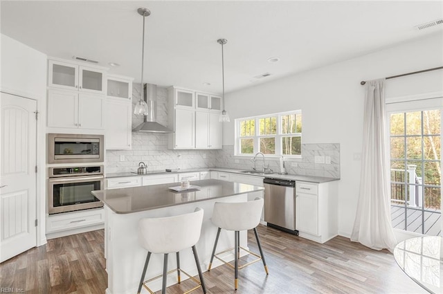 kitchen featuring wall chimney range hood, white cabinetry, backsplash, stainless steel appliances, and a kitchen island