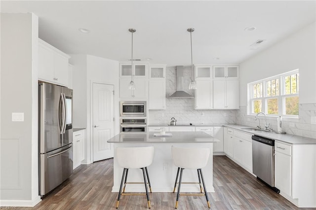 kitchen with wall chimney exhaust hood, white cabinetry, appliances with stainless steel finishes, and a center island