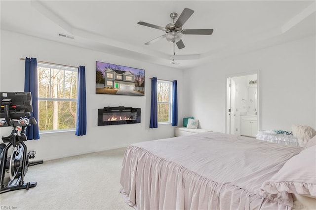 bedroom featuring multiple windows, a tray ceiling, light carpet, and ceiling fan