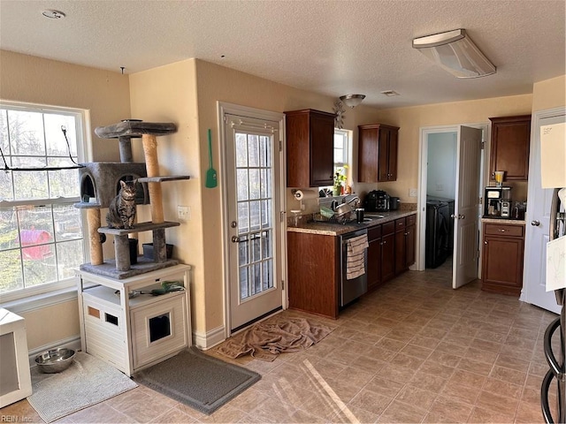 kitchen with independent washer and dryer, stainless steel dishwasher, sink, and a textured ceiling