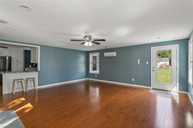 unfurnished living room featuring dark wood-type flooring, ceiling fan, sink, and a wall mounted air conditioner