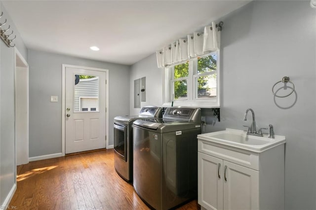 clothes washing area with washing machine and dryer, electric panel, light hardwood / wood-style flooring, and sink