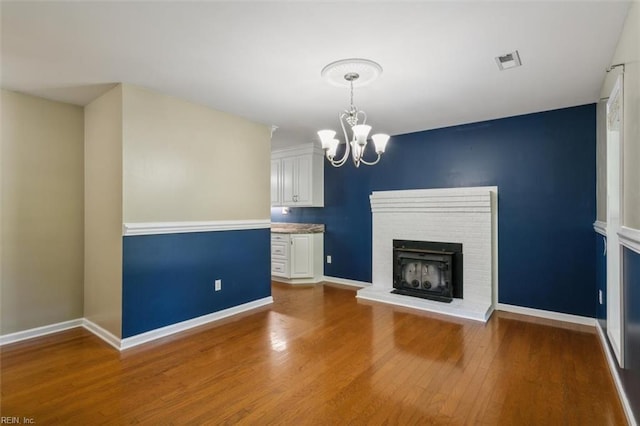 unfurnished living room with a fireplace, wood-type flooring, and a notable chandelier