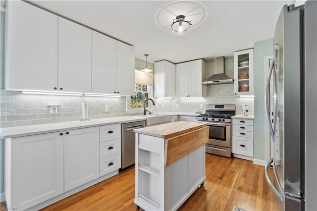 kitchen featuring wall chimney range hood, pendant lighting, stainless steel appliances, and white cabinetry