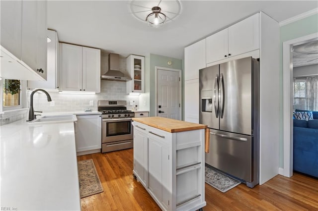 kitchen featuring butcher block countertops, appliances with stainless steel finishes, backsplash, wall chimney range hood, and white cabinets