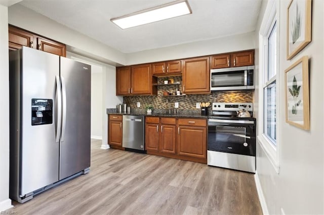 kitchen featuring stainless steel appliances, dark stone counters, tasteful backsplash, light hardwood / wood-style floors, and sink