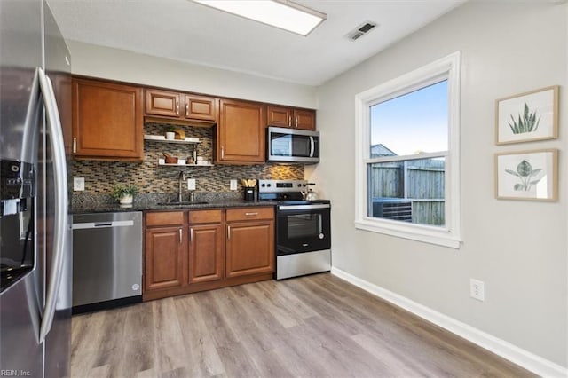 kitchen featuring decorative backsplash, sink, light hardwood / wood-style flooring, stainless steel appliances, and dark stone counters