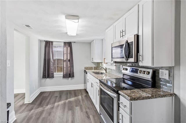 kitchen featuring sink, light hardwood / wood-style flooring, dark stone countertops, stainless steel appliances, and white cabinets