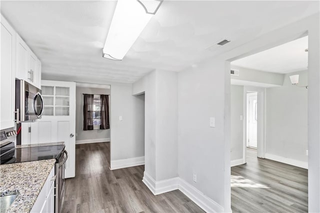 kitchen with white cabinetry, appliances with stainless steel finishes, light stone countertops, and hardwood / wood-style flooring