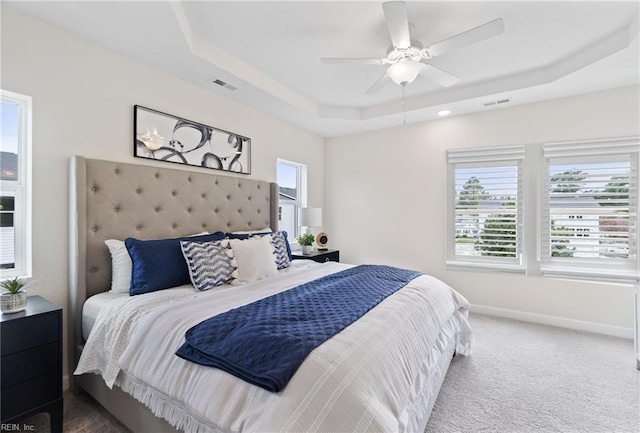 carpeted bedroom with ceiling fan and a raised ceiling