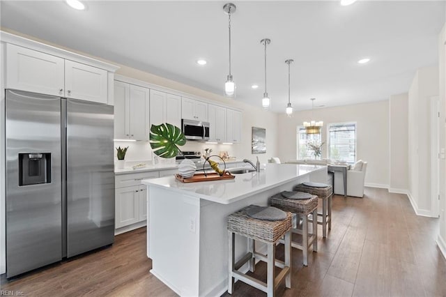 kitchen featuring white cabinetry, an island with sink, a breakfast bar area, appliances with stainless steel finishes, and decorative light fixtures