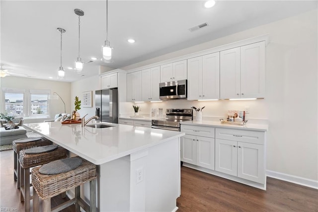 kitchen featuring appliances with stainless steel finishes, white cabinets, a center island with sink, and hanging light fixtures