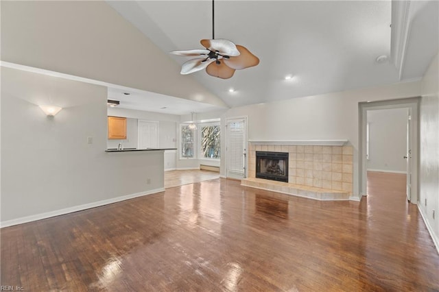 unfurnished living room with ceiling fan, light wood-type flooring, a tile fireplace, and high vaulted ceiling