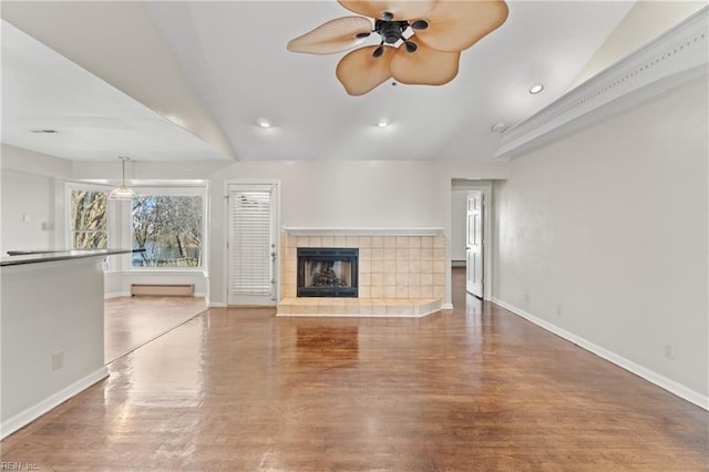 unfurnished living room featuring ceiling fan, vaulted ceiling, a tile fireplace, and hardwood / wood-style flooring