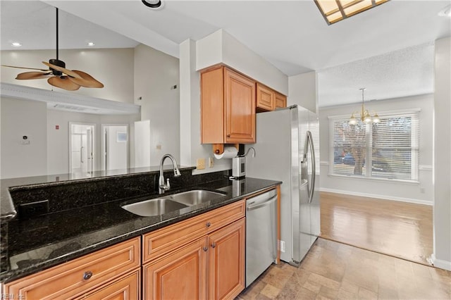 kitchen with ceiling fan with notable chandelier, appliances with stainless steel finishes, decorative light fixtures, dark stone countertops, and sink