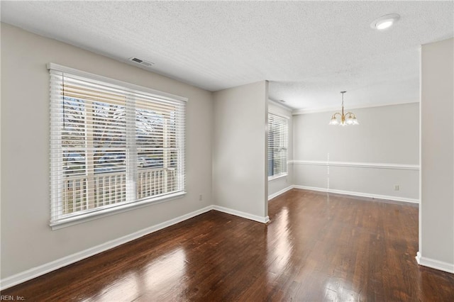 unfurnished room featuring dark wood-type flooring, a textured ceiling, and a chandelier