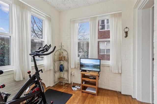 exercise area with brick wall, hardwood / wood-style floors, and a textured ceiling