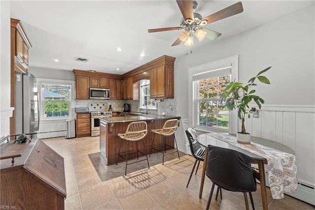 kitchen with light tile patterned floors, kitchen peninsula, a breakfast bar area, appliances with stainless steel finishes, and decorative backsplash