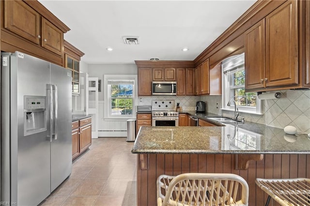 kitchen with dark stone countertops, kitchen peninsula, sink, stainless steel appliances, and a baseboard radiator