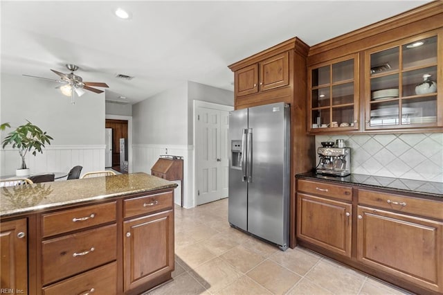 kitchen with light tile patterned floors, stainless steel fridge, ceiling fan, backsplash, and dark stone counters