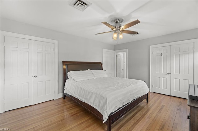 bedroom with ceiling fan, light wood-type flooring, and two closets