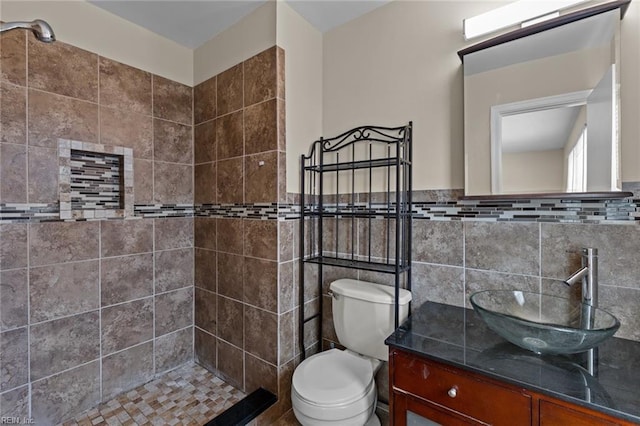 bathroom featuring tile walls, vanity, toilet, and a tile shower