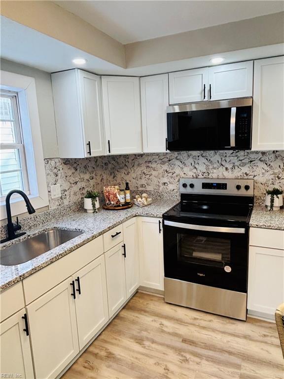 kitchen with appliances with stainless steel finishes, sink, white cabinets, light stone countertops, and light hardwood / wood-style floors