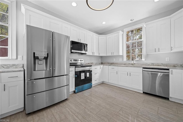 kitchen featuring light stone countertops, white cabinets, appliances with stainless steel finishes, and sink