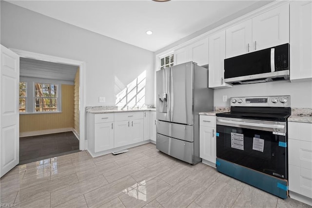 kitchen with stainless steel appliances, white cabinetry, and light stone counters