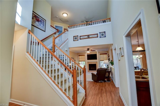 stairs with a high ceiling, sink, wood-type flooring, and ceiling fan with notable chandelier