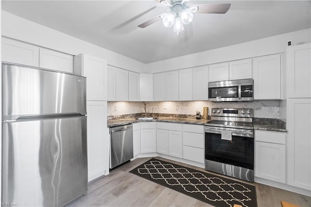 kitchen featuring light hardwood / wood-style floors, white cabinets, dark stone countertops, backsplash, and stainless steel appliances