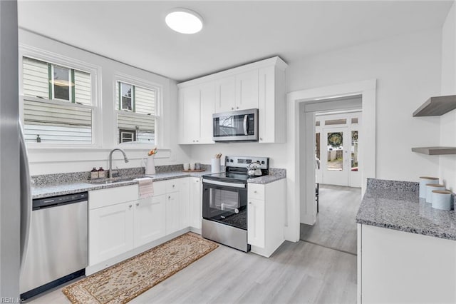 kitchen with light stone countertops, white cabinets, light hardwood / wood-style flooring, and stainless steel appliances