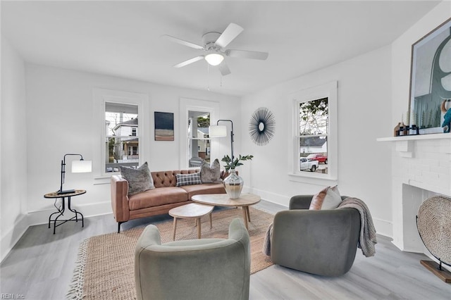 living room with ceiling fan, a brick fireplace, and light hardwood / wood-style flooring