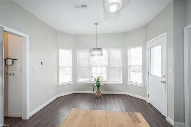 unfurnished dining area featuring dark wood-type flooring, plenty of natural light, and a chandelier