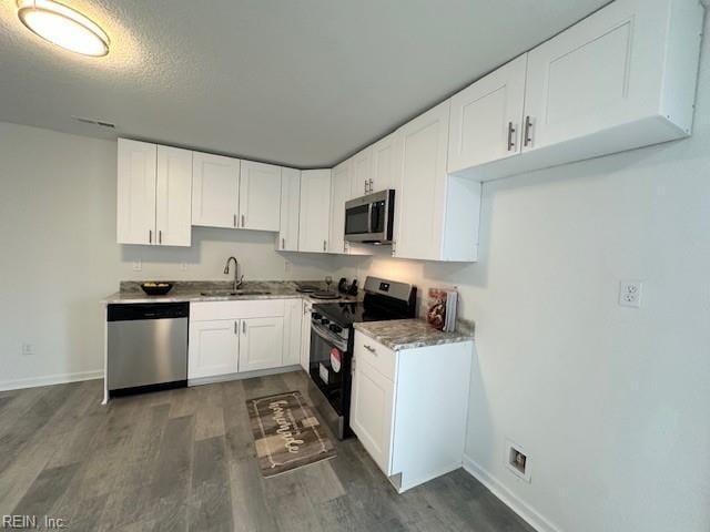 kitchen with appliances with stainless steel finishes, a textured ceiling, white cabinets, sink, and dark hardwood / wood-style floors