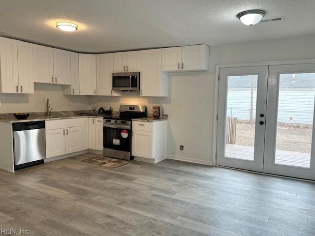 kitchen featuring white cabinetry, appliances with stainless steel finishes, light hardwood / wood-style flooring, and a textured ceiling