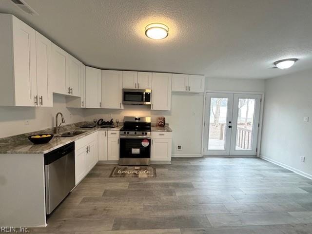 kitchen featuring appliances with stainless steel finishes, sink, white cabinetry, dark stone counters, and a textured ceiling