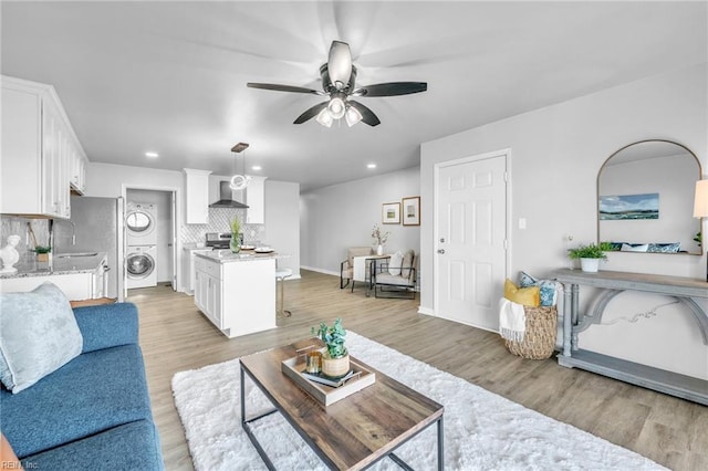 living room with stacked washer / drying machine, light hardwood / wood-style floors, and ceiling fan