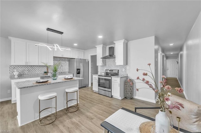 kitchen with pendant lighting, appliances with stainless steel finishes, white cabinetry, light stone countertops, and wall chimney exhaust hood