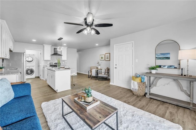 living room with stacked washer and clothes dryer, light wood-type flooring, and ceiling fan