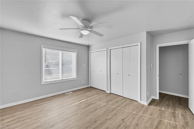 unfurnished bedroom featuring two closets, light hardwood / wood-style floors, and ceiling fan