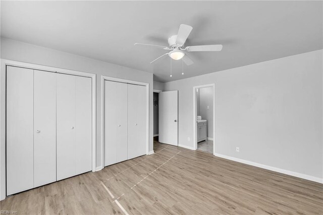 unfurnished bedroom with ensuite bath, light hardwood / wood-style floors, ceiling fan, and two closets