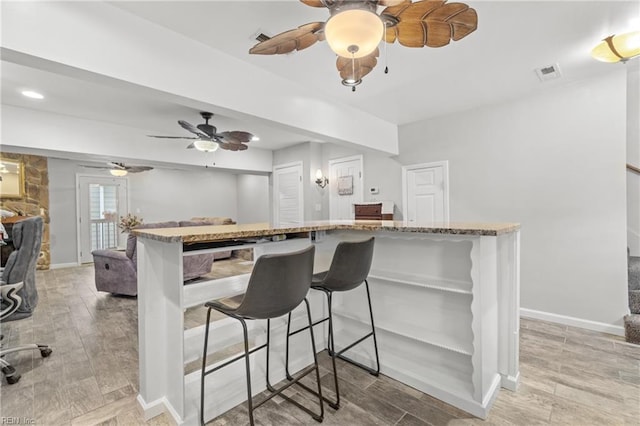 kitchen featuring kitchen peninsula, a kitchen bar, a fireplace, and ceiling fan