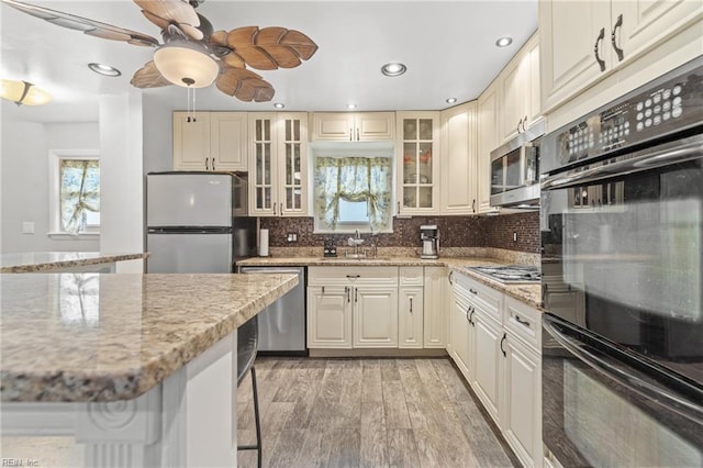 kitchen featuring light stone countertops, appliances with stainless steel finishes, a breakfast bar area, light hardwood / wood-style floors, and cream cabinetry